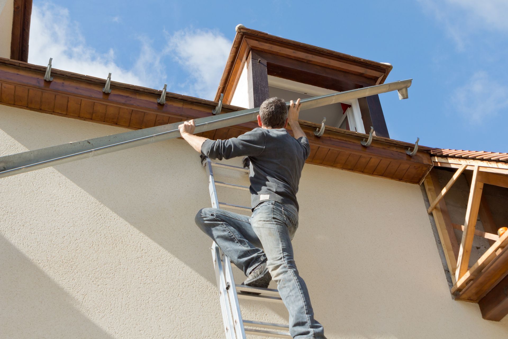 Une personne monte à une échelle pour travailler sur le toit d'une maison sous un avant-toit en bois