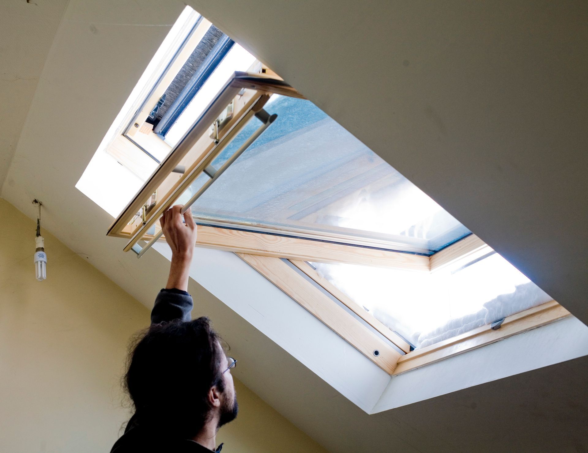 Une personne ouvre une fenêtre de toit dans un plafond incliné, laissant entrer la lumière du jour.