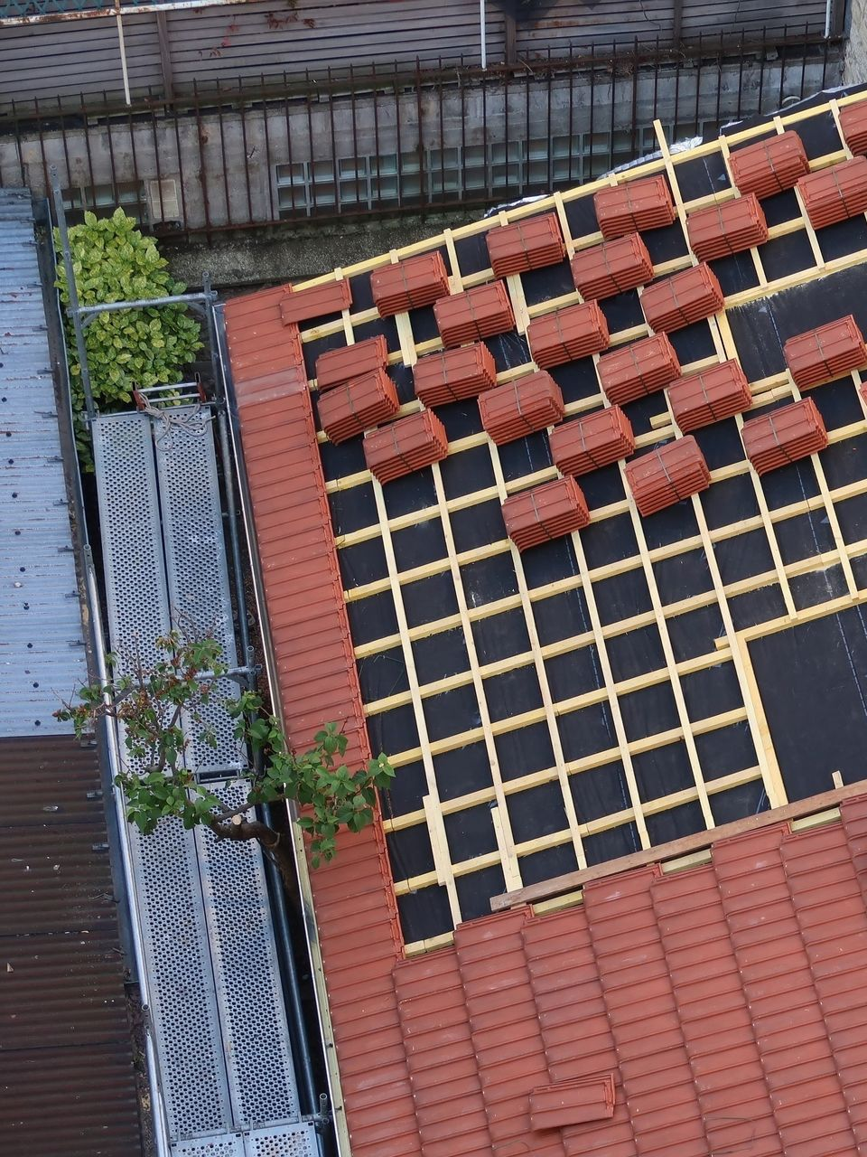 Toit-terrasse avec tuiles rouges, grille en treillis noir et petits pots de plantes en bord de toit