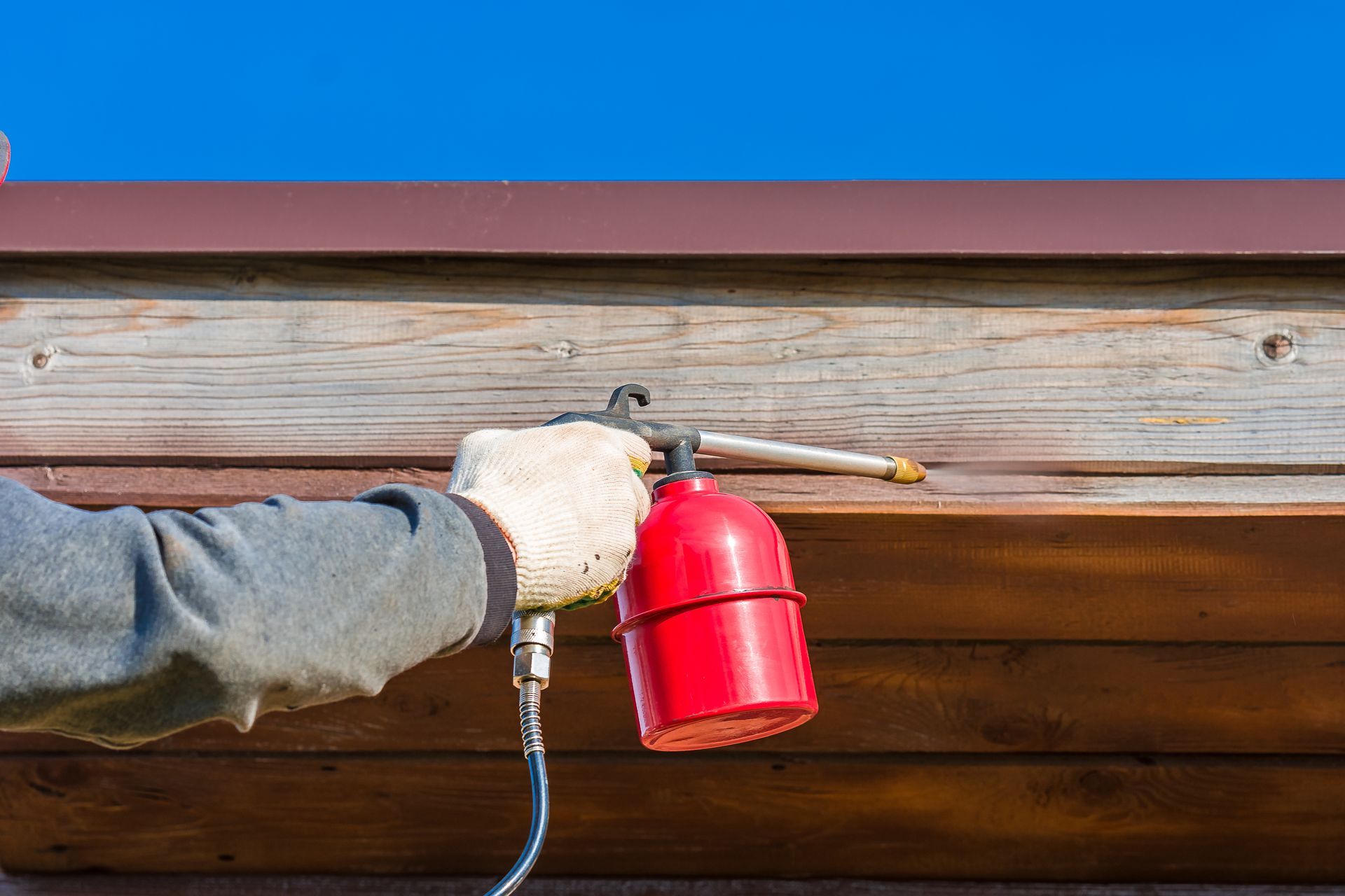 Main gantée utilisant un extincteur rouge pour pulvériser sous un avant-toit en bois