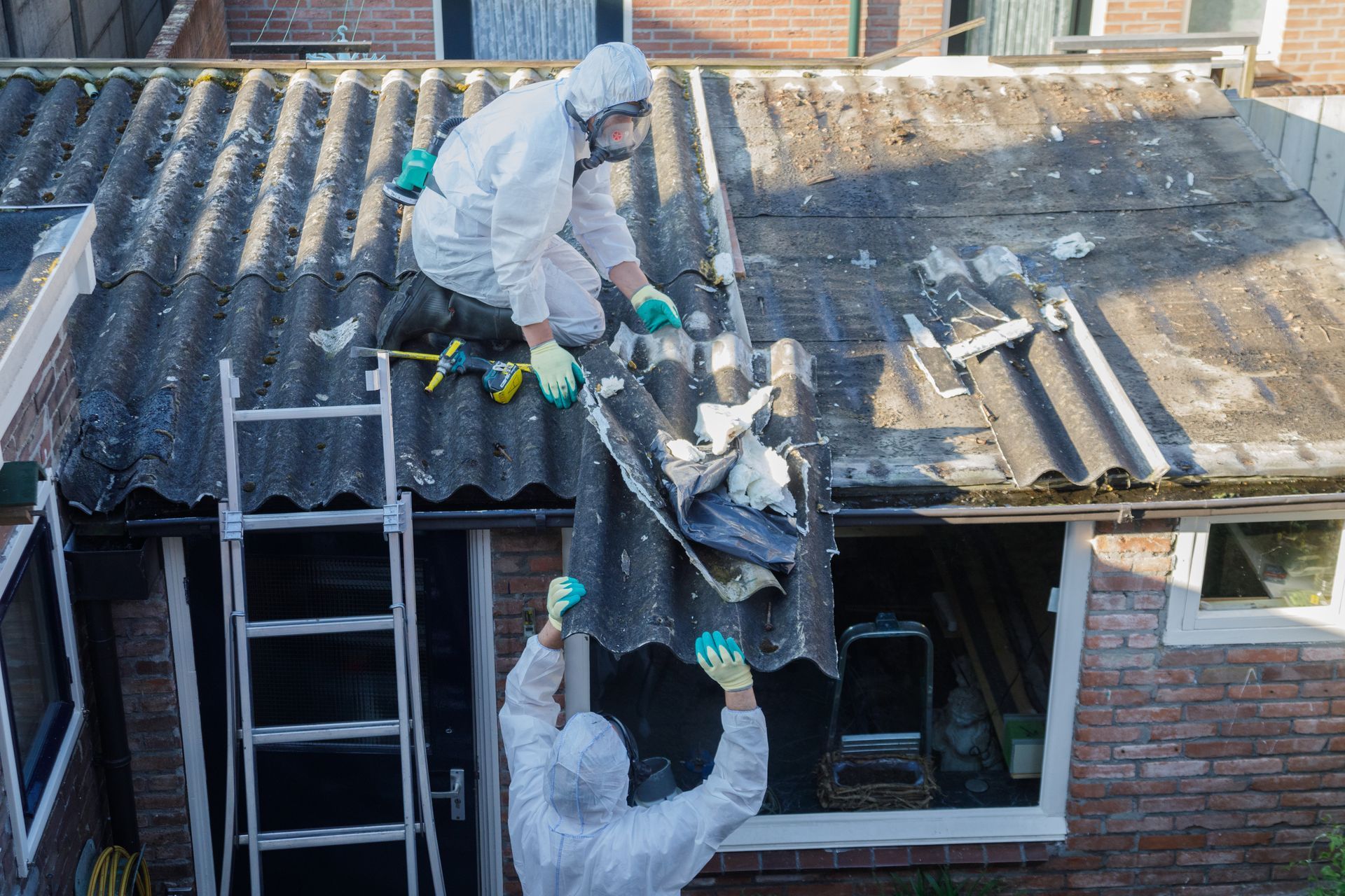Des ouvriers en combinaisons de protection décontaminent un toit d'amiante.