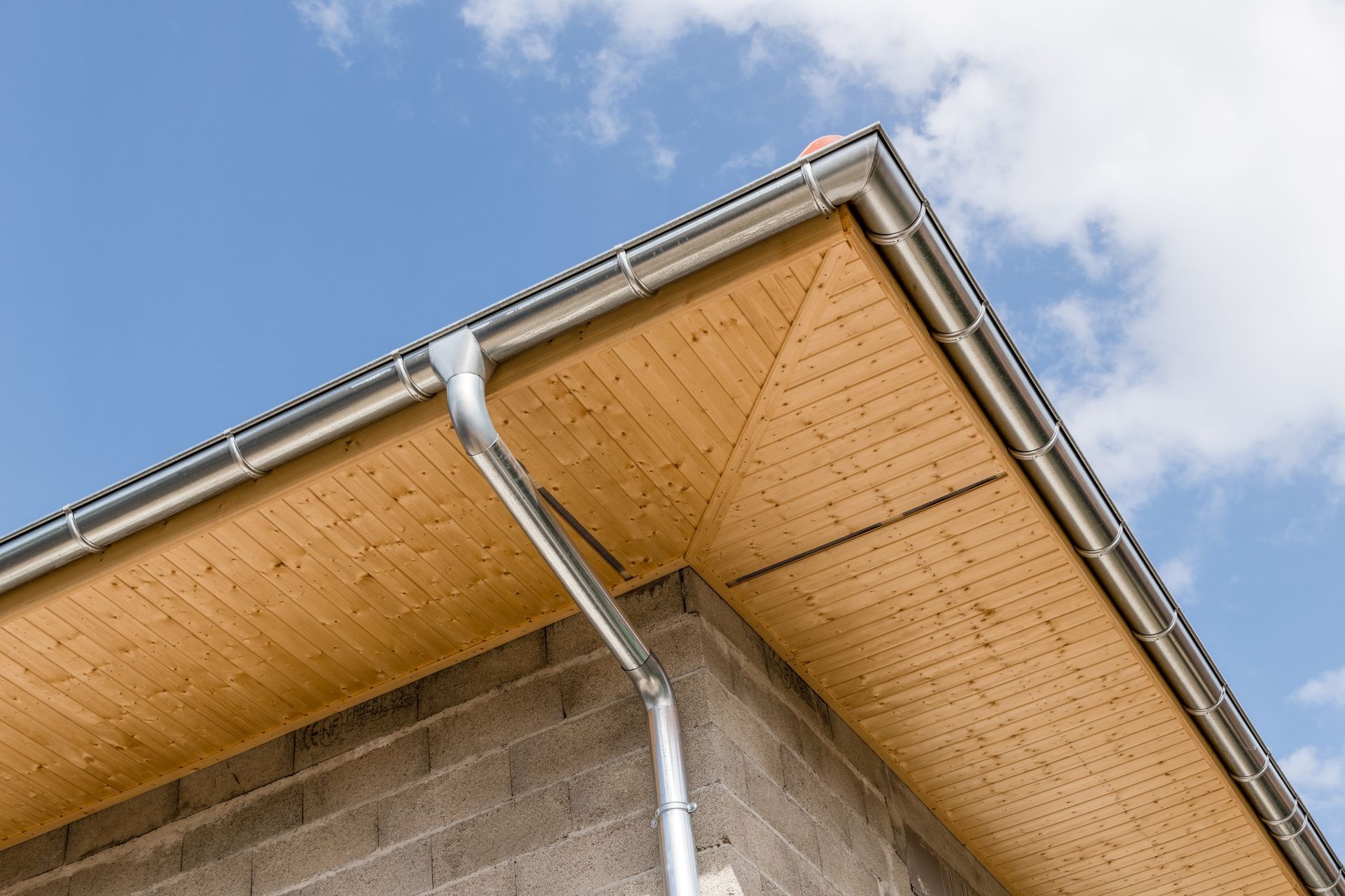 Gros plan sur un coin de toit de maison avec une gouttière et une descente pluviale en métal sur fond de ciel bleu