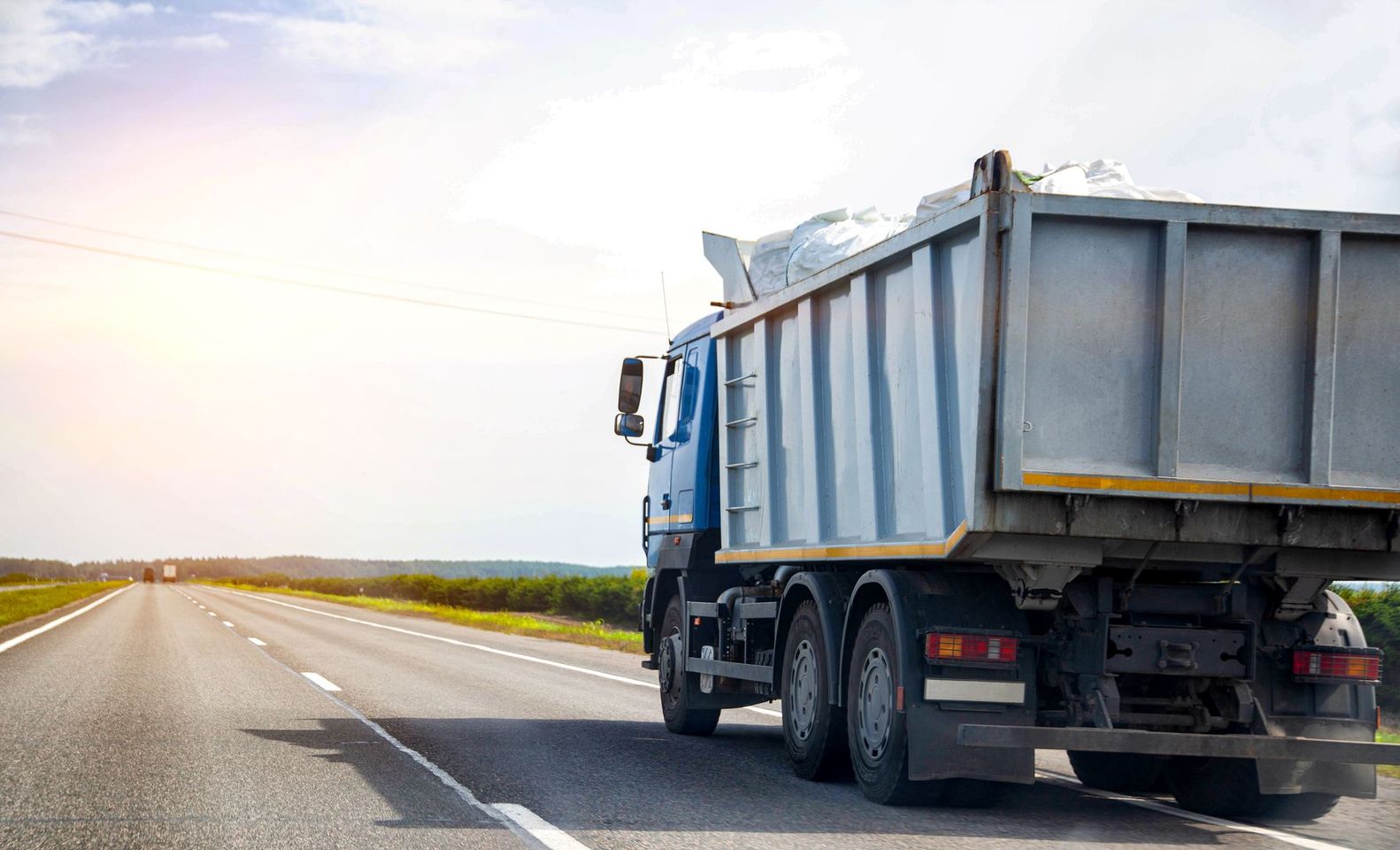 Camion-benne bleu circule sur une autoroute sous un ciel lumineux.