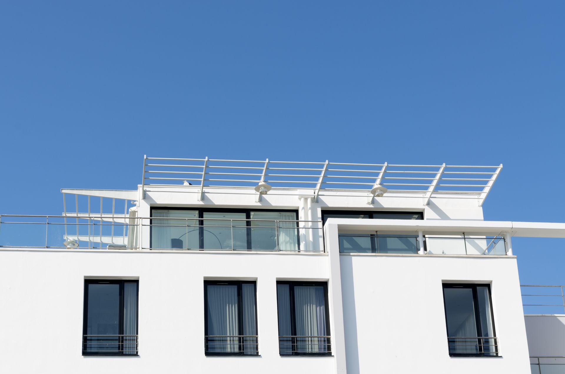 Immeuble d'appartements blanc moderne avec balcons vitrés et pergola sur le toit se détachant sur un ciel bleu
