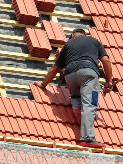 Ouvrier installant des tuiles rouges sur un toit de tuiles pentu