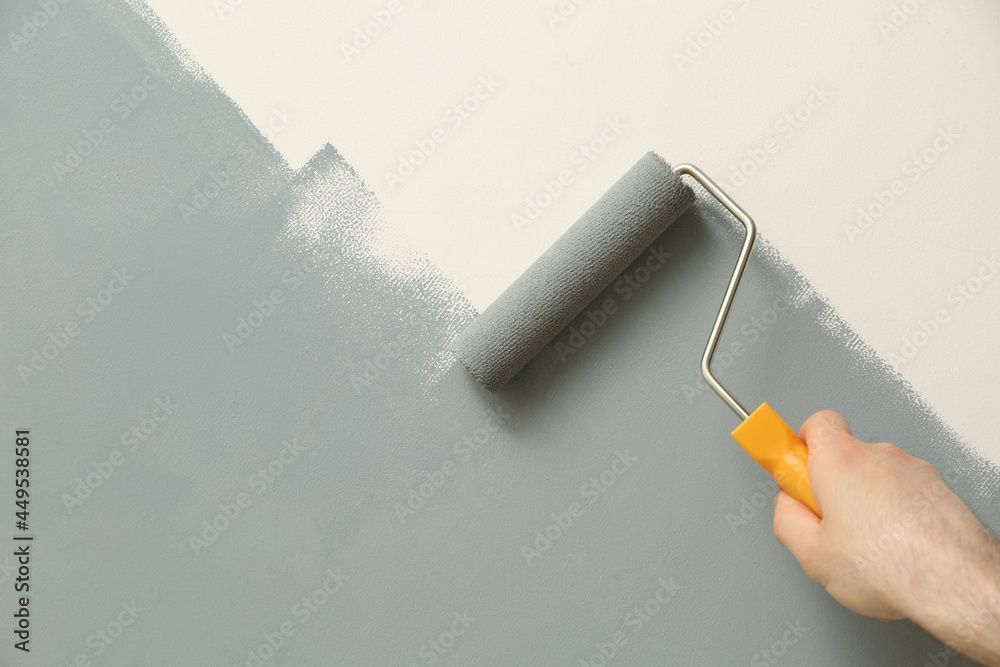 Eine hellgraue Wand mit einer Farbrolle von Hand streichen.