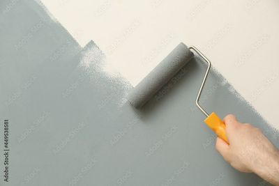 Eine hellgraue Wand mit einer Farbrolle von Hand streichen.