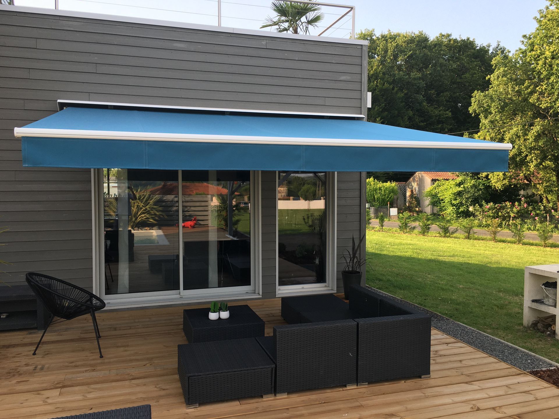 Une terrasse en bois meublée avec un store bleu