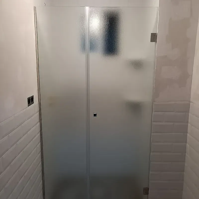 Un baño con puerta de ducha de vidrio esmerilado y azulejos blancos.