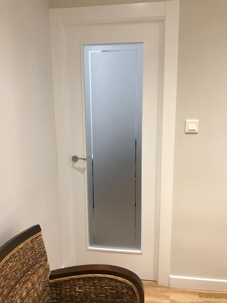Una puerta blanca con una ventana de vidrio esmerilado en una habitación con una silla.