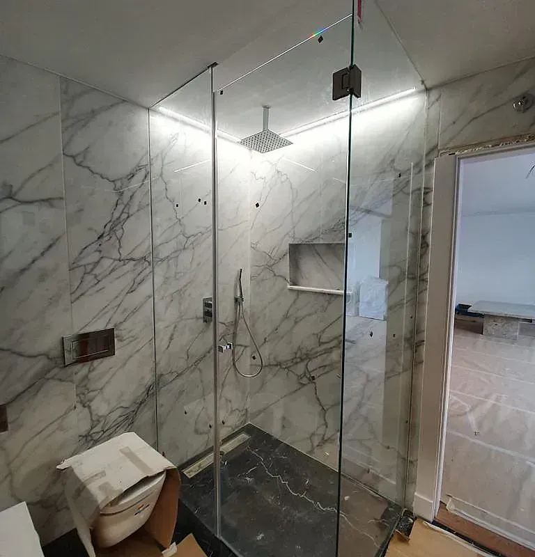 Un baño con paredes de mármol y ducha a ras de suelo con puerta de cristal.