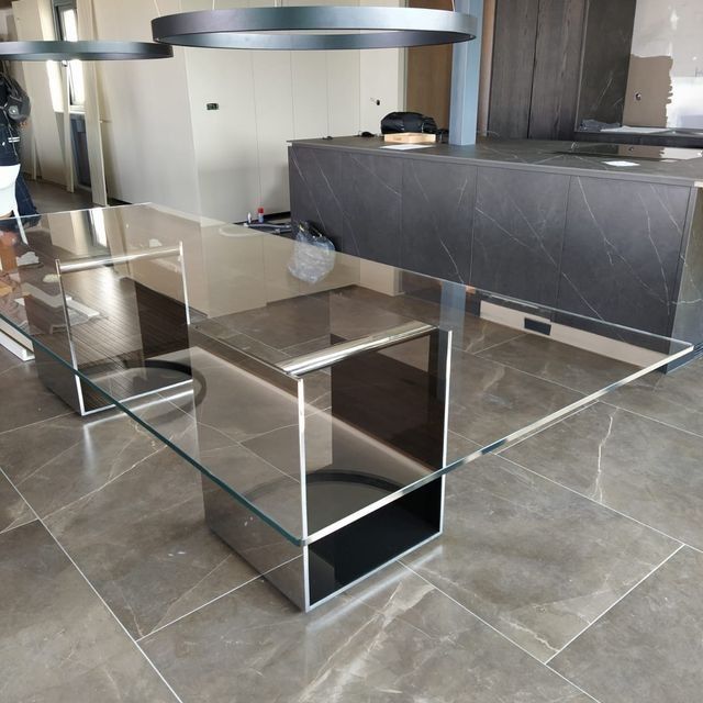 Una mesa de vidrio con base de acero inoxidable se encuentra sobre un piso de baldosas.