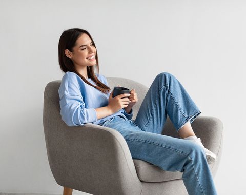 Femme souriante assise dans un fauteuil, une tasse de café dans les mains