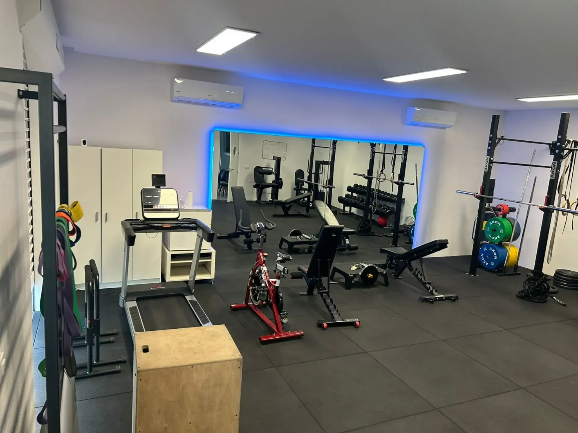 Un gimnasio con cinta de correr, bicicleta estática, bancos y un espejo.