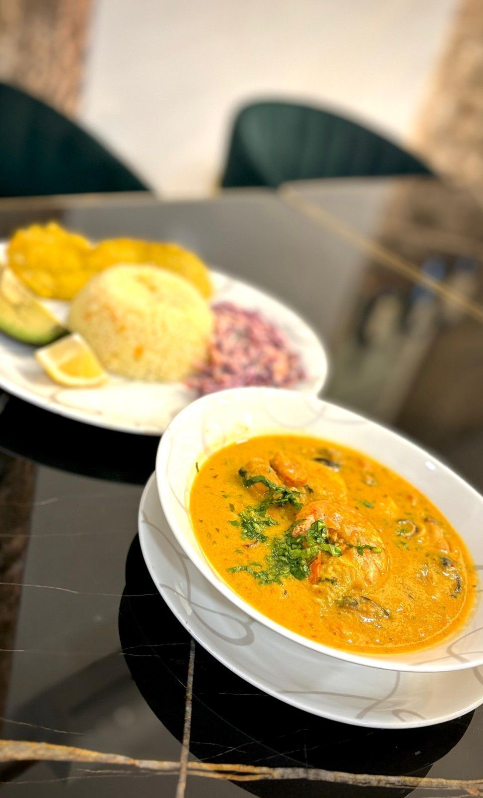 Un tazón de guiso de mariscos con naranja, arroz, plátanos y ensalada sobre una mesa negra.