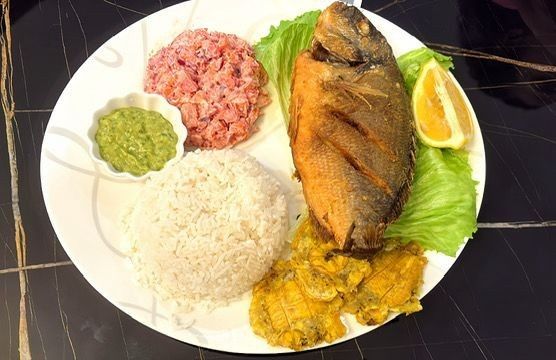 Plato de pescado frito, arroz, carne rosada, salsa verde, plátano amarillo y limón.