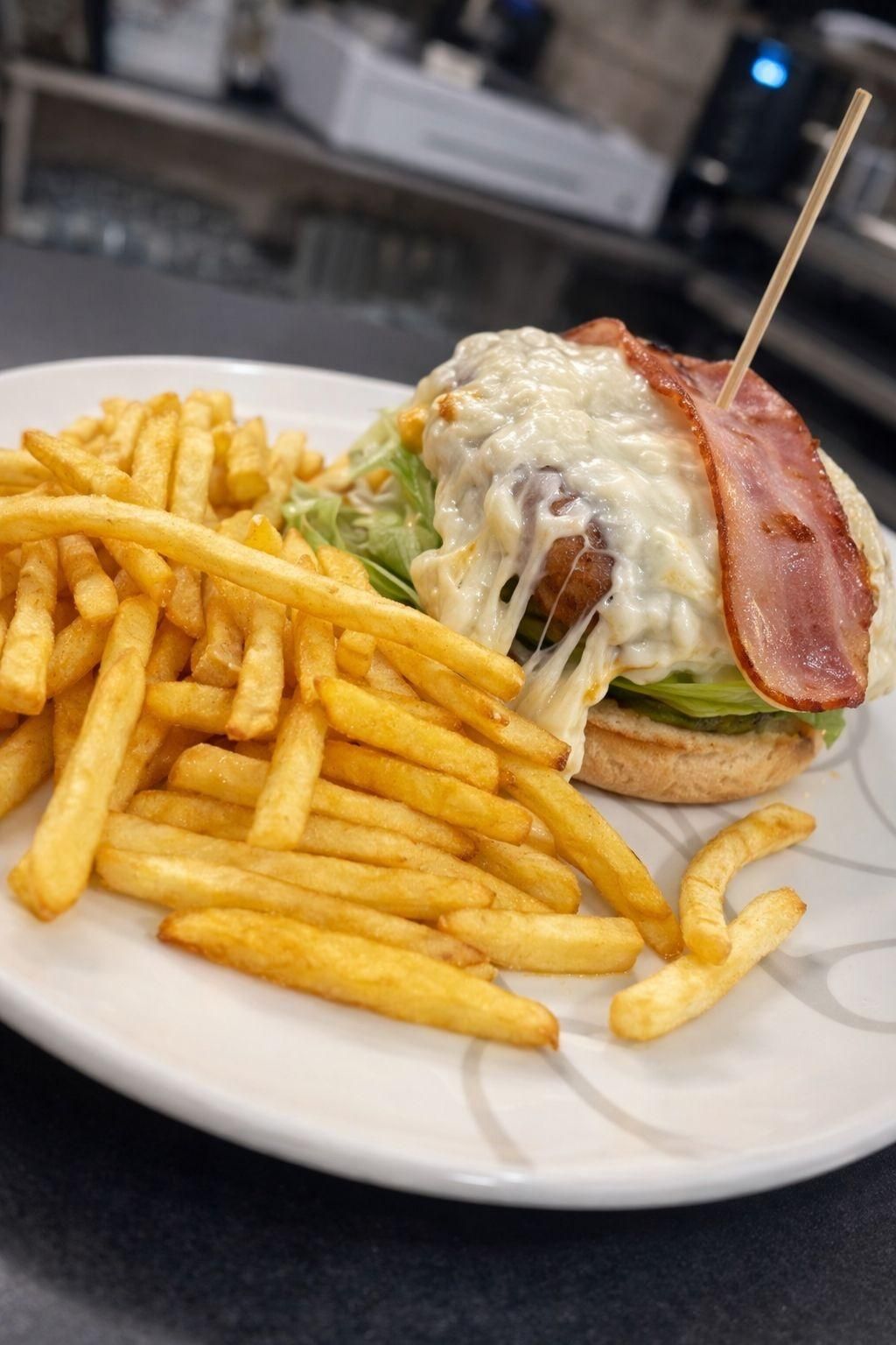 Hamburguesa con tocino y queso derretido, servida con papas fritas en un plato blanco.