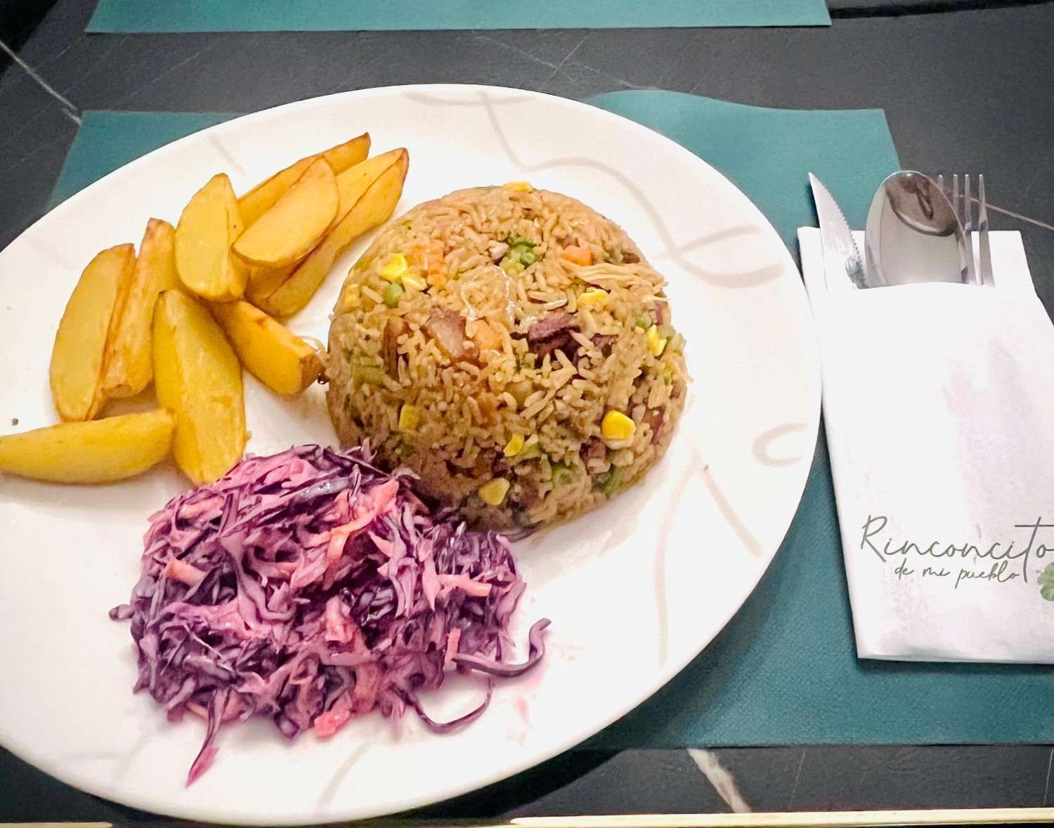 Plato de arroz frito, patatas gajo y ensalada de col con servilleta y cubiertos.