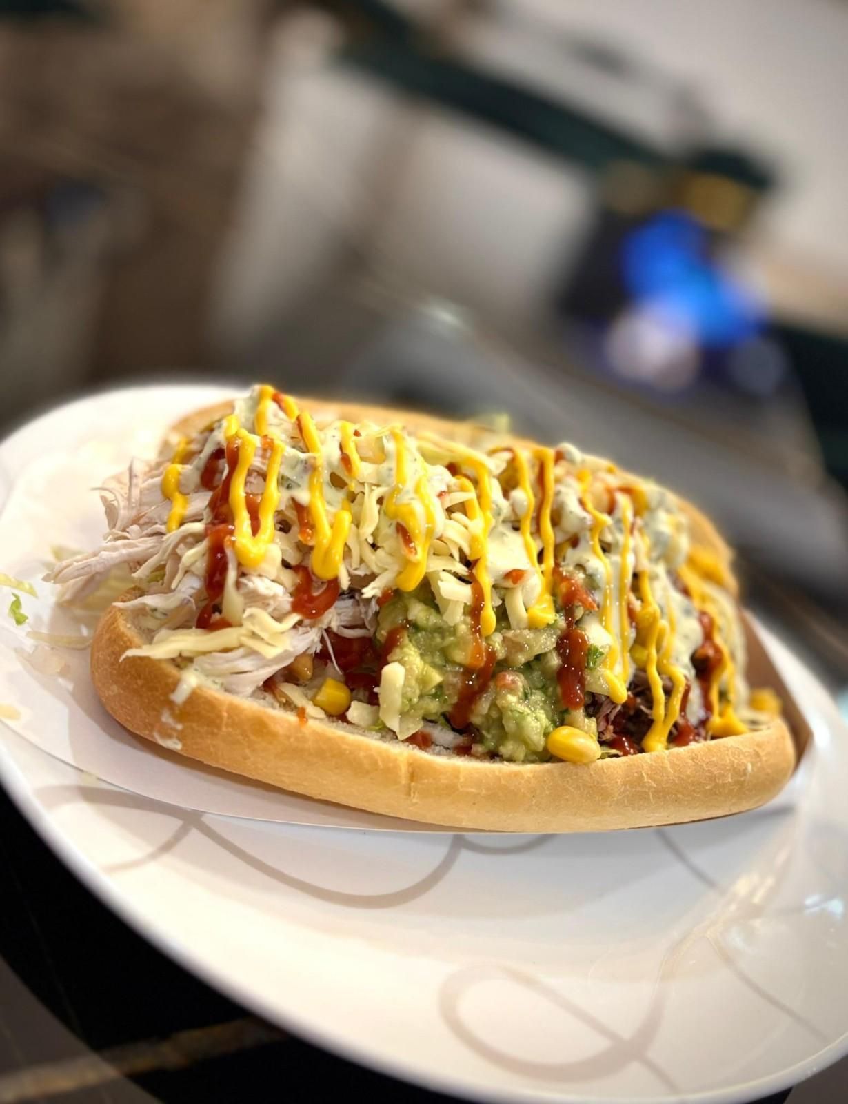 Un sándwich con queso en un plato blanco. Incluye guacamole, salsa de queso y un chorrito de salsa.