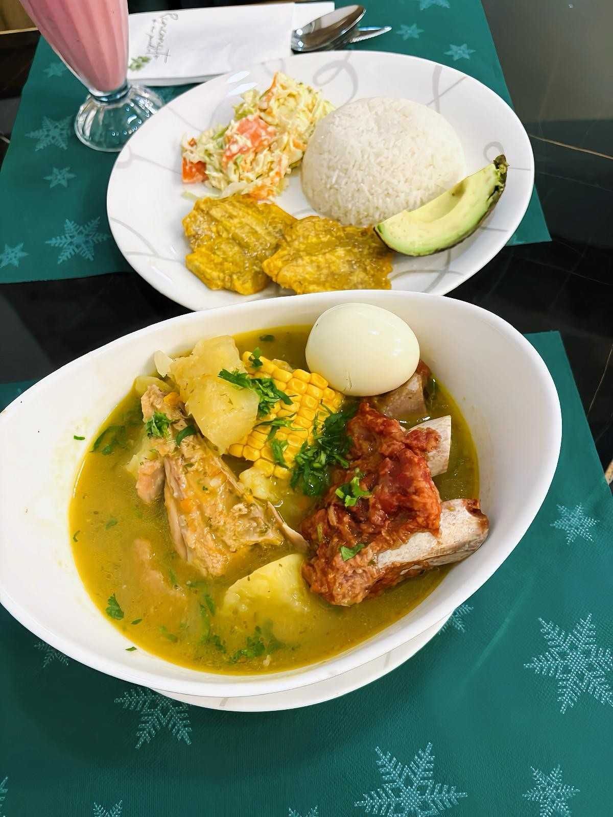 Sopa de cerdo, papas y maíz, servida con arroz, plátanos, aguacate y ensalada.