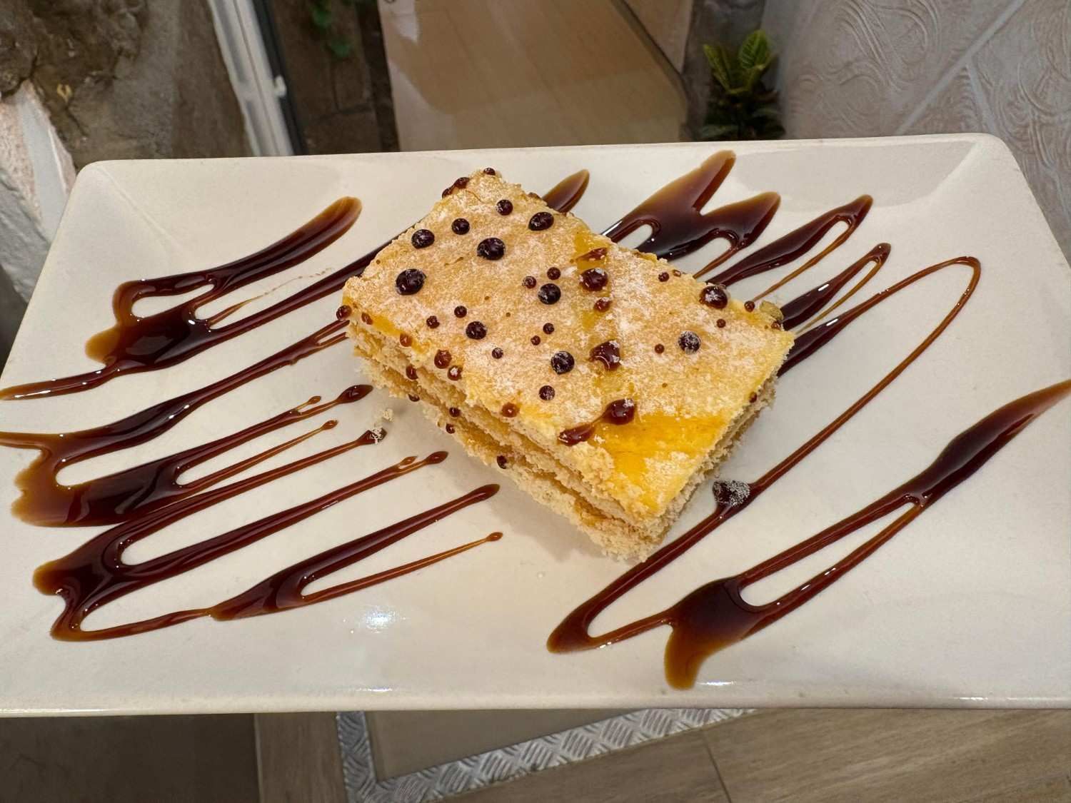 Rebanada de pastel en plato blanco, rociada con salsa de chocolate y decorada con puntos de chocolate negro.