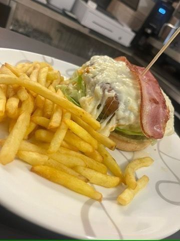 Hamburguesa con papas fritas en un plato. Lleva queso, tocino y lechuga. Un palillo la mantiene unida.