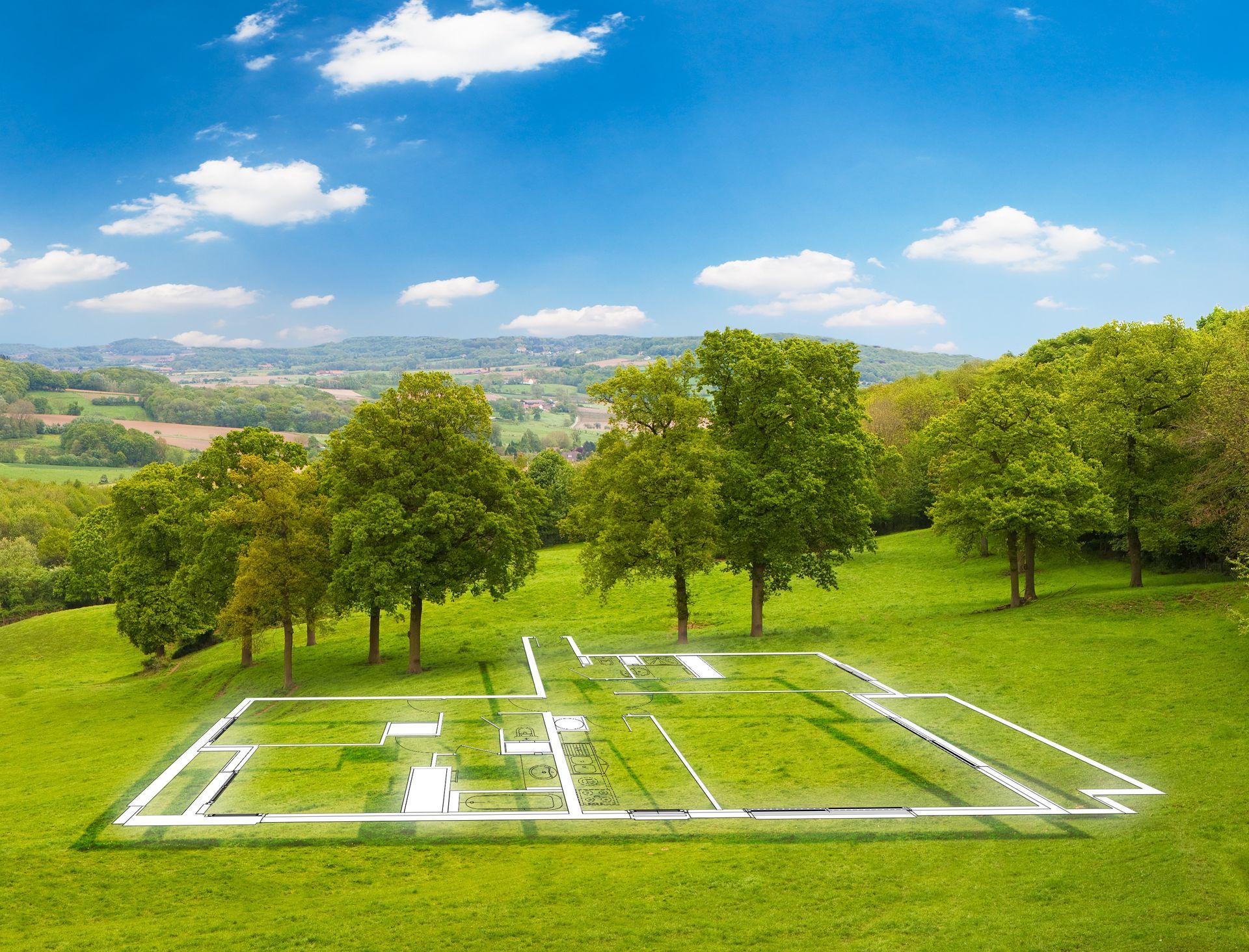 Champ herbeux avec les contours blancs des fondations d'une maison, entourés d'arbres sous un ciel bleu.