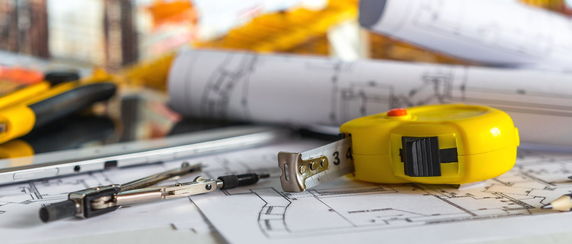 Outils de dessin et ruban à mesurer sur des plans architecturaux.
