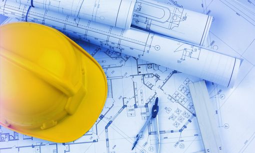 Casque jaune sur des plans architecturaux bleus et des dessins techniques.