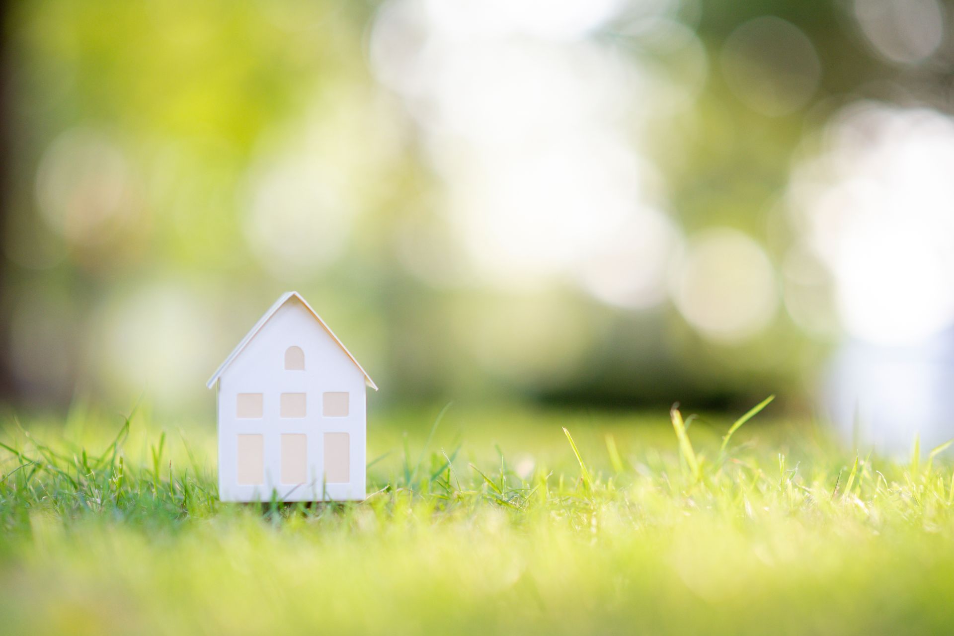 Maquette d'une petite maison blanche sur fond d'herbe verte avec un arrière-plan ensoleillé flou.