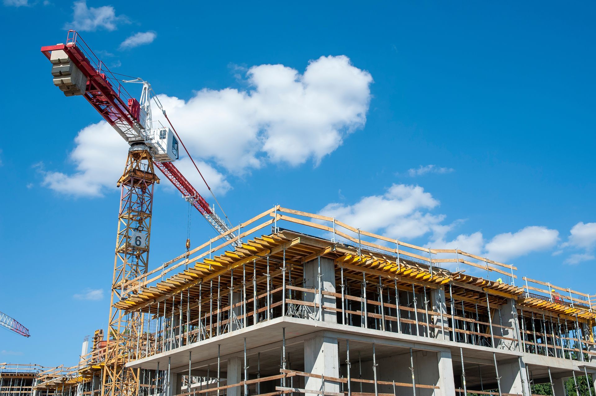 Chantier de construction avec une grue surplombant un bâtiment en construction, le tout se détachant sur un ciel bleu.