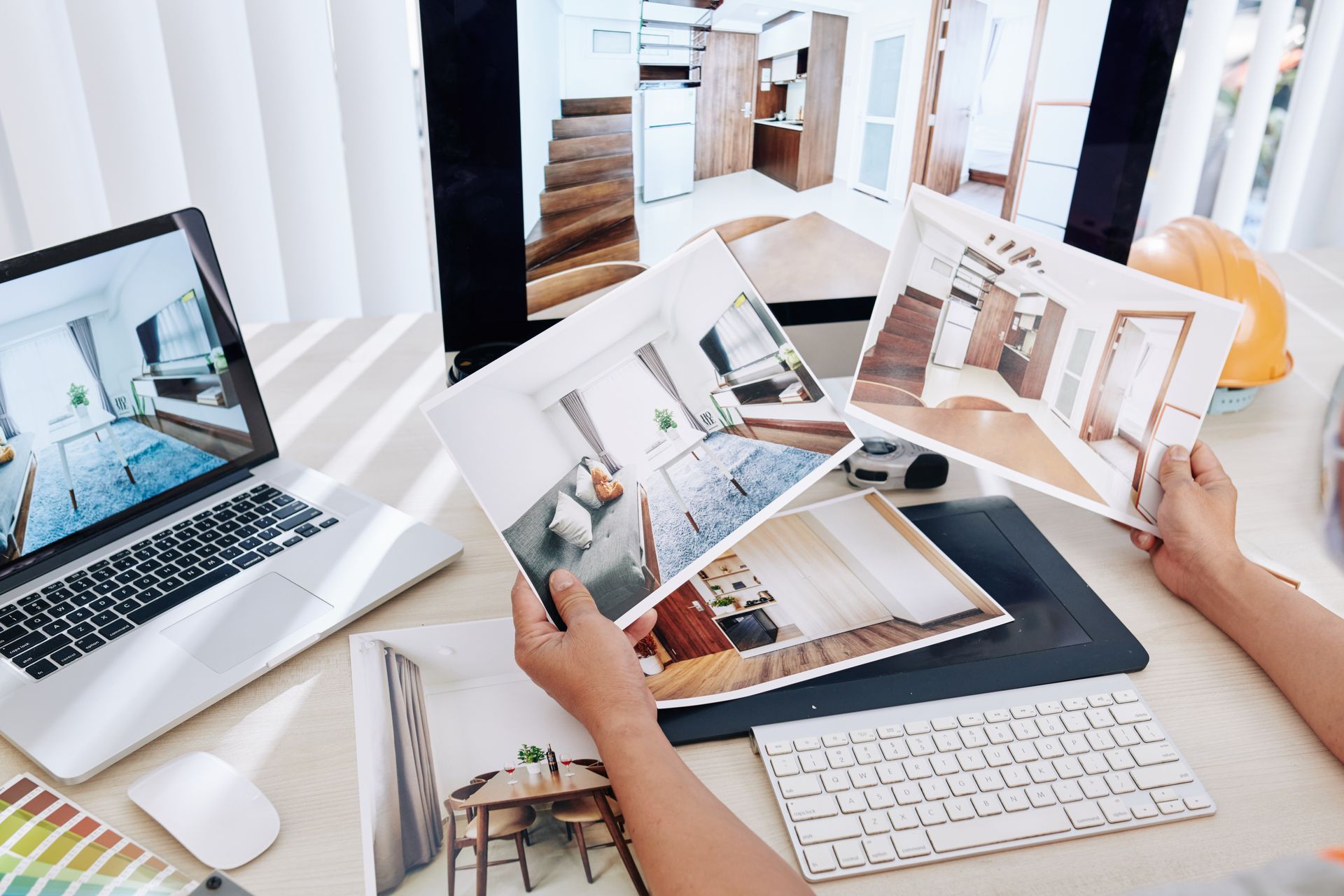 Des mains examinent des photos d'architecture et des maquettes d'ordinateurs portables sur un bureau lumineux.
