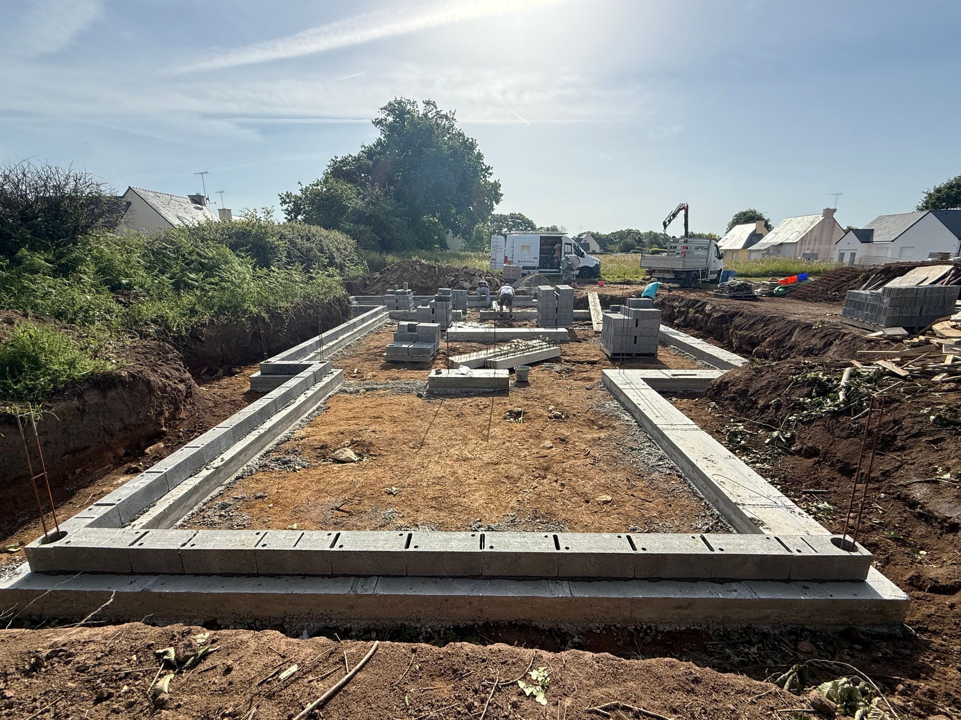 Deux ouvriers du bâtiment en tenue de sécurité se tiennent devant un chantier avec des excavatrices et des camions-bennes derrière eux.