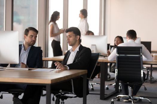 Un grupo de personas están sentadas en escritorios en una oficina trabajando con computadoras.