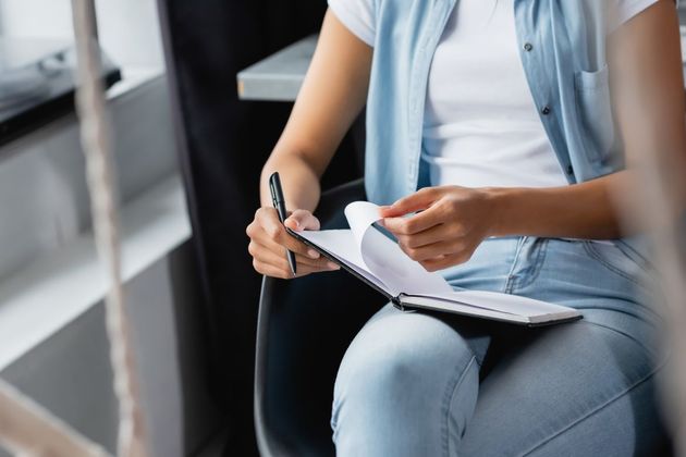 Una mujer está sentada en una silla escribiendo en un cuaderno.