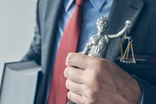 Un hombre con traje y corbata sostiene una estatua de la justicia.
