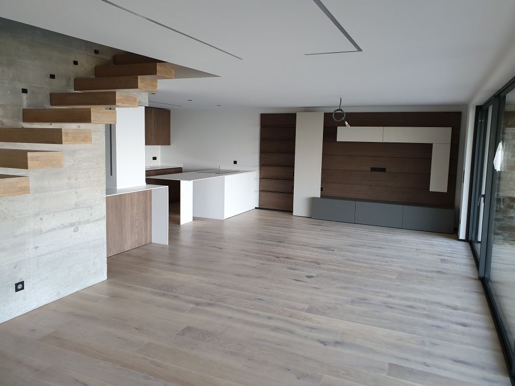 Espace salle à manger, cuisine ouverte et lumineuse avec parquet, murs blancs, table et portes coulissantes en verre.