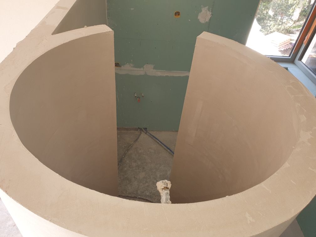 Cloison incurvée en plaques de plâtre beiges formant une petite pièce circulaire en construction à l'intérieur.