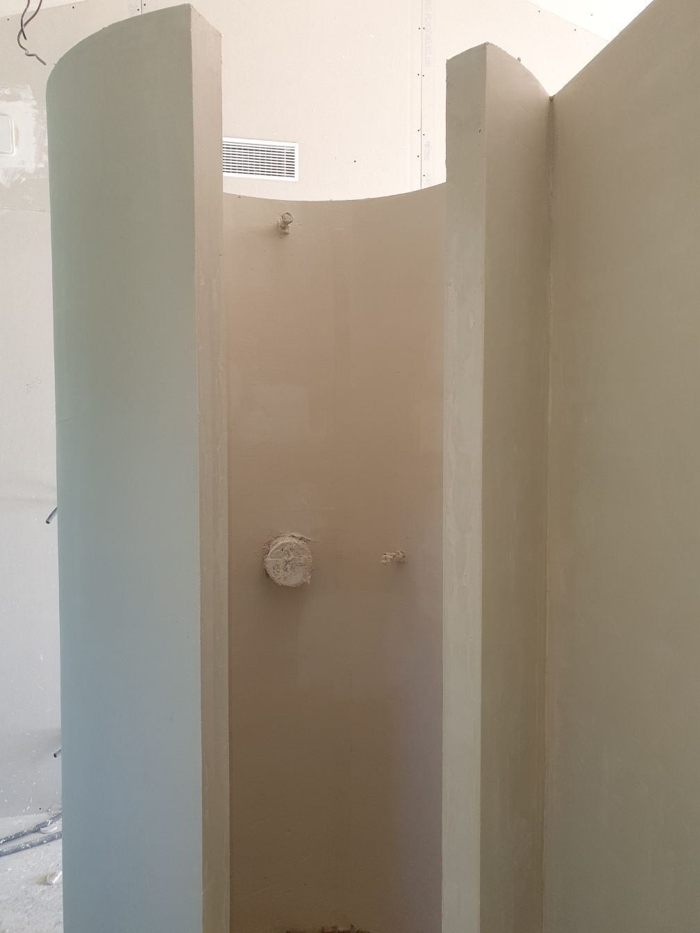 Cabine de douche extérieure beige avec parois incurvées et pommeau de douche.