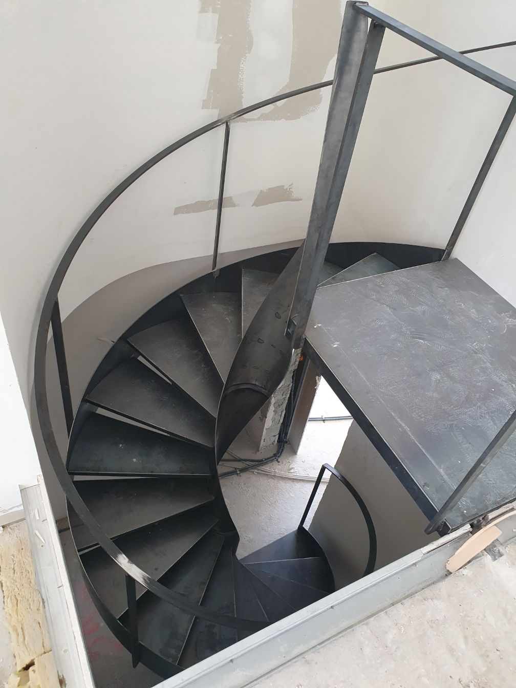 Escalier en colimaçon avec marches noires et rampe métallique dans une cage d'escalier intérieure étroite.