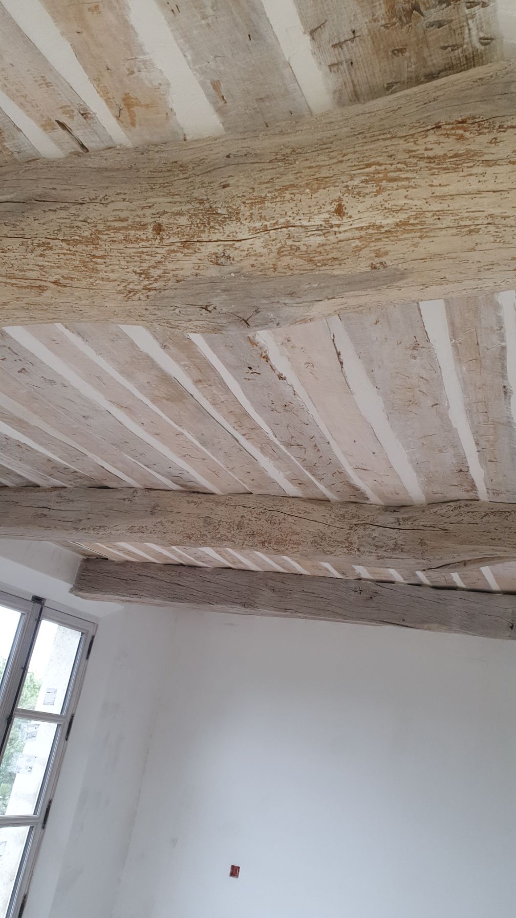Plafond avec poutres apparentes et peinture écaillée dans une pièce peu meublée.