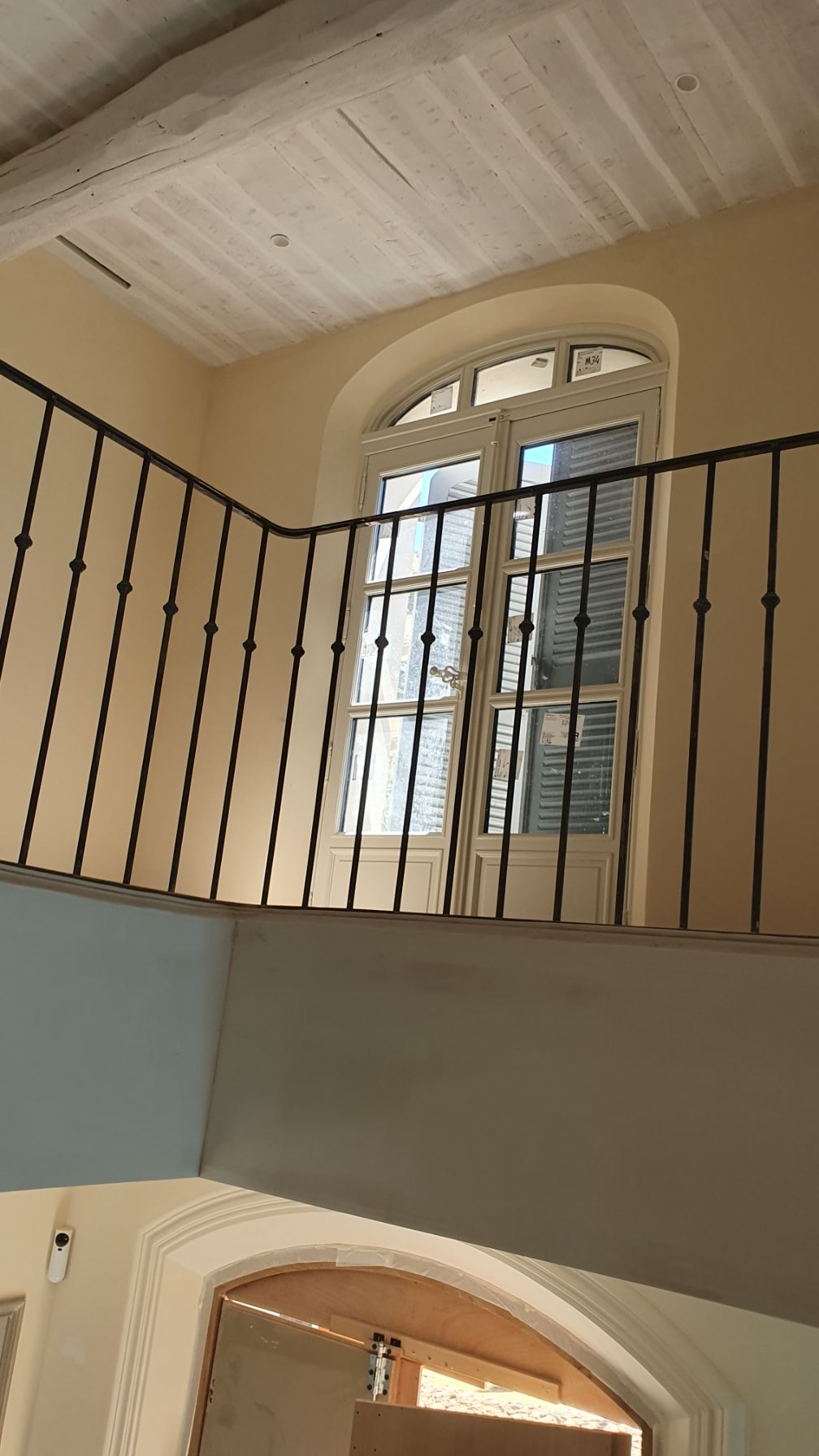 Palier d'escalier incurvé avec rampe en fer noir, fenêtres cintrées et murs et plafond couleur crème.
