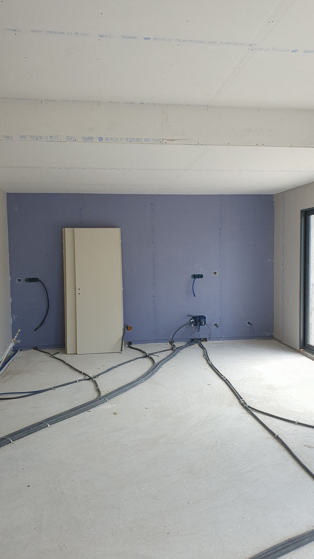 Pièce vide en rénovation, avec des murs bleus, un sol blanc et des câbles apparents au sol.
