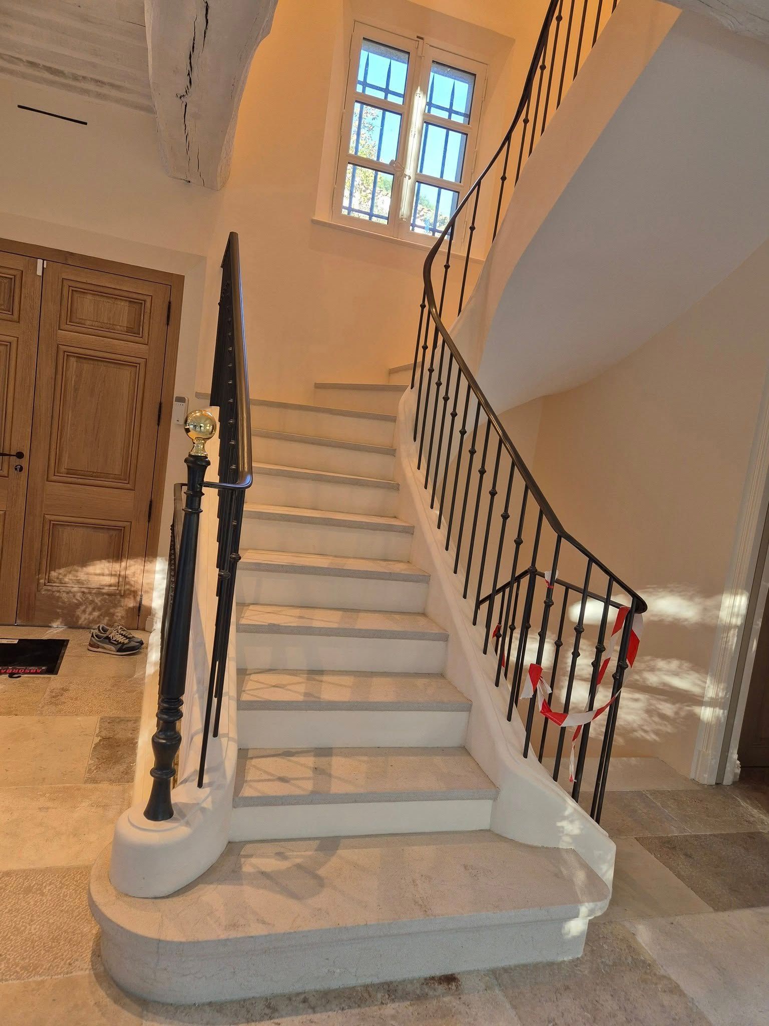 Escalier intérieur avec marches blanches, rampe foncée et palier éclairé par une fenêtre dans un couloir beige.