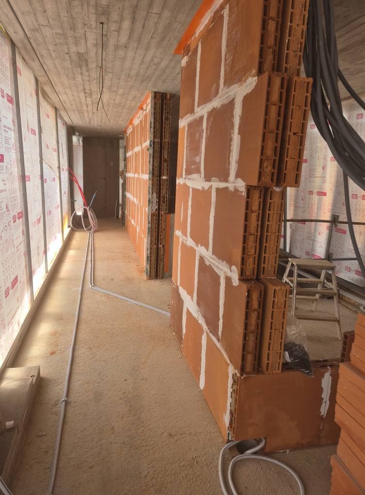 Couloir étroit et inachevé avec murs en briques, plafond en béton et matériaux de construction au sol.