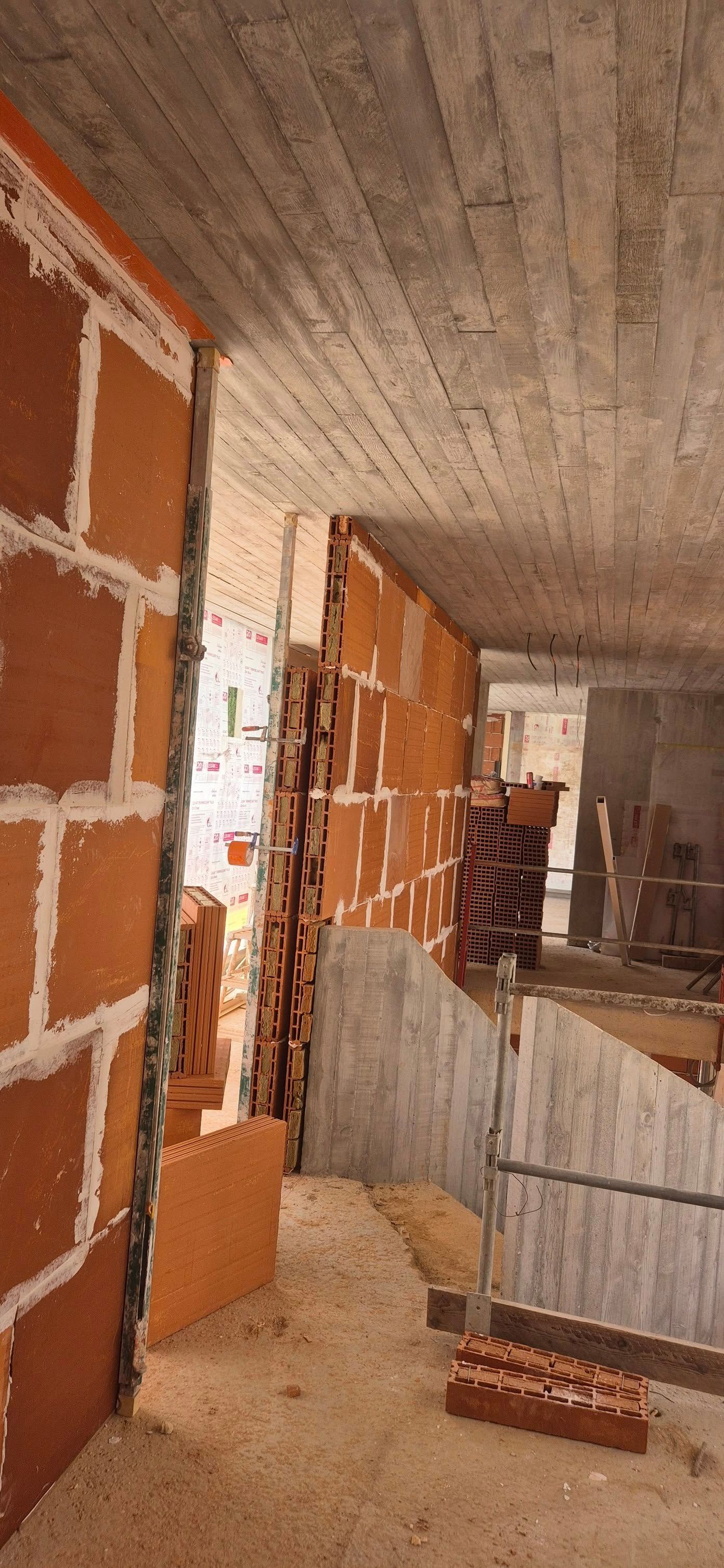 Intérieur partiellement aménagé avec murs en briques apparentes, plafond en béton et débris de construction au sol.