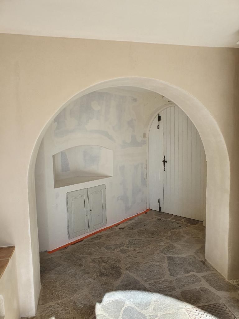 Alcôve cintrée avec cloisons sèches non finies, porte blanche et sol carrelé imitation pierre dans une pièce en rénovation.