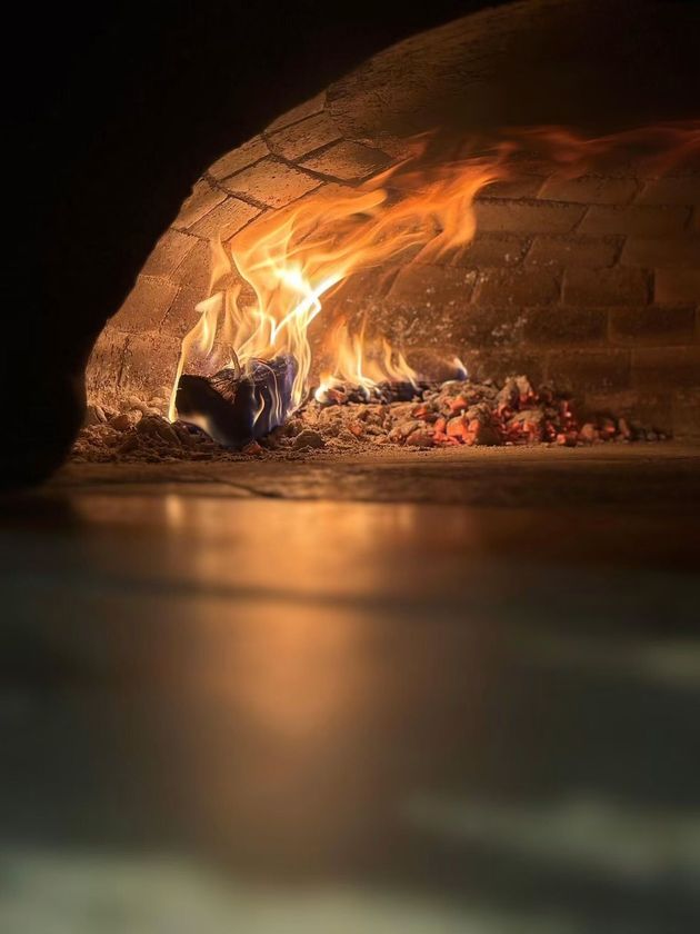 Pizza cuite au feu de bois dans un four en briques, les flammes illuminant la croûte