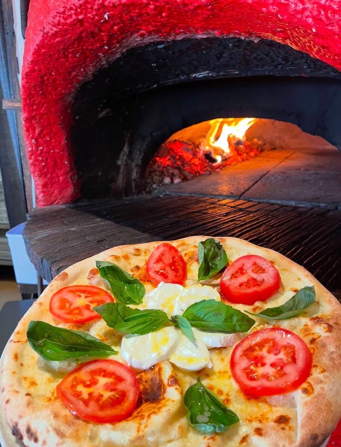 Pizza aux tomates et au basilic cuite dans un four à bois, avec des flammes qui rougeoient à l'intérieur.