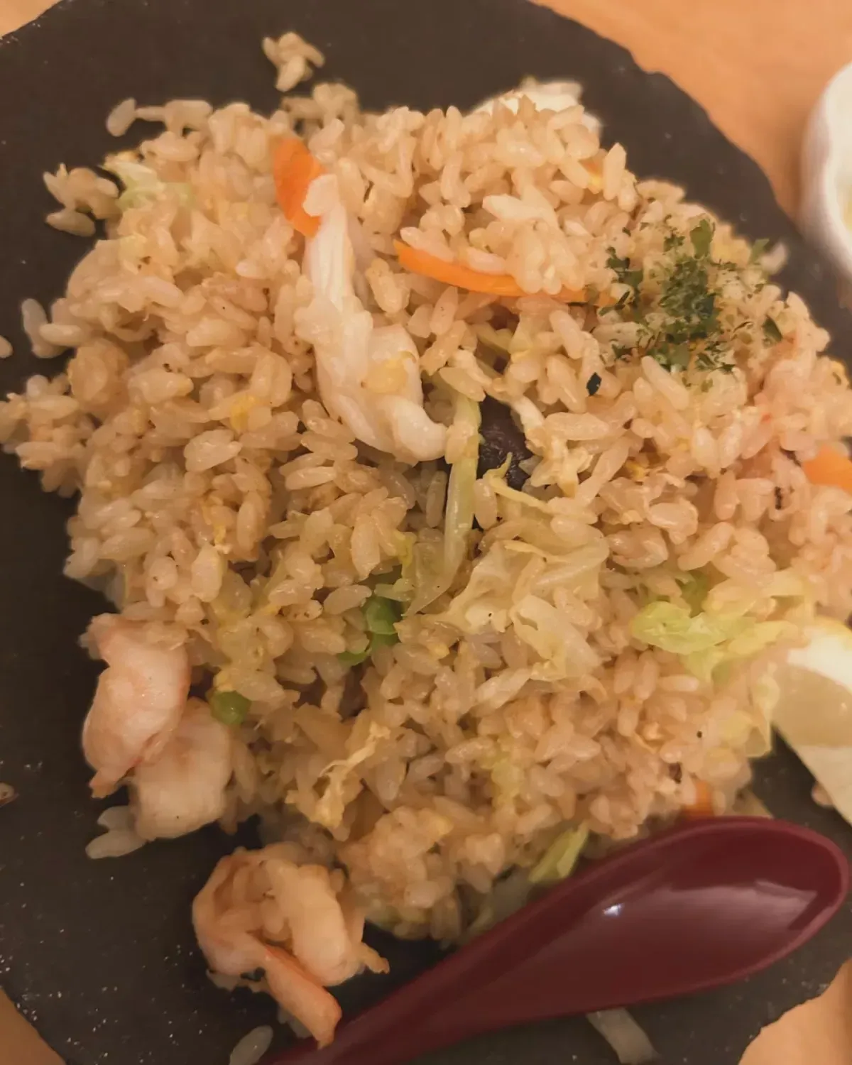 Arroz frito con camarones, zanahorias y repollo en un plato negro, con una cuchara roja.